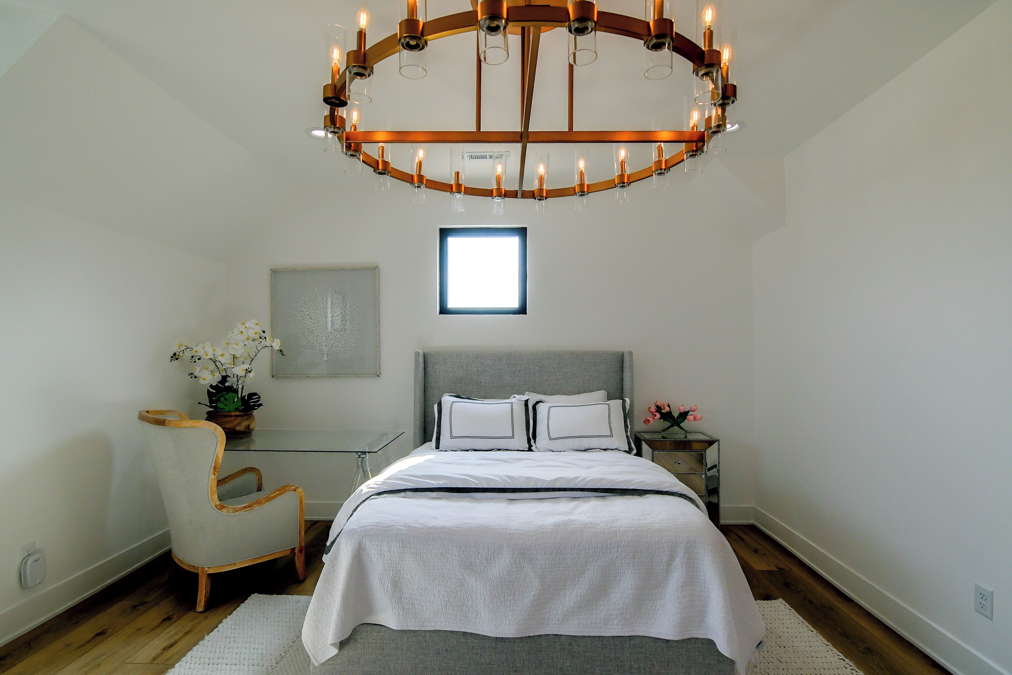A bedroom with a large bed, a chair, a nightstand, a mirror, and a chandelier.