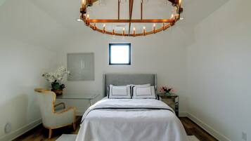A bedroom with a large bed, a chair, a nightstand, a mirror, and a chandelier.