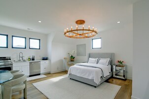 Un dormitorio moderno con una cama grande, un comedor con mesa de vidrio y una cocina con armarios blancos.