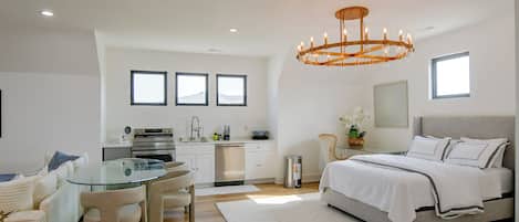 Un dormitorio moderno con una cama grande, una mesa de comedor de vidrio y una cocina al fondo.