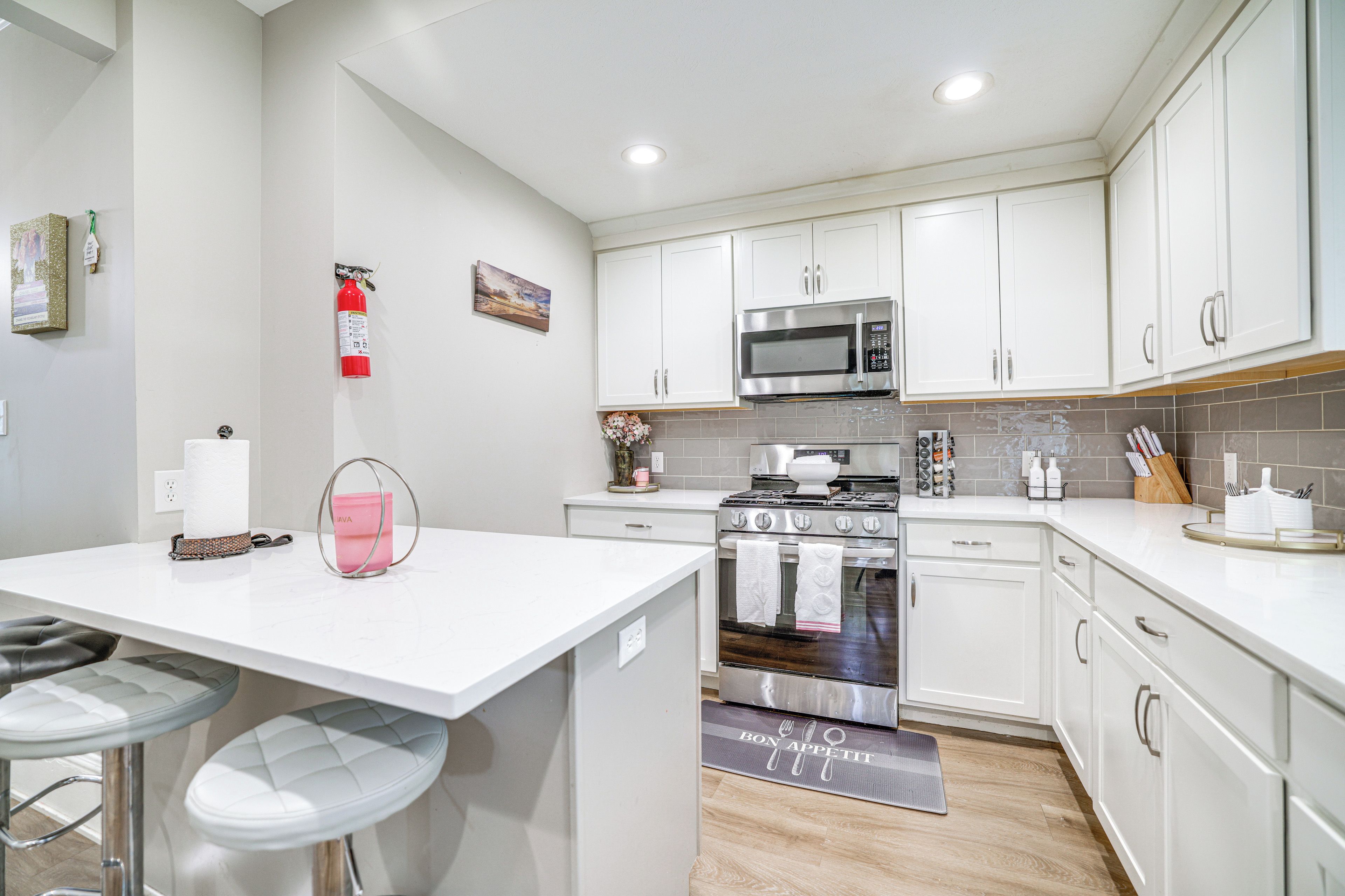 A modern kitchen with white cabinets, stainless steel appliances, and a bar area with stools.