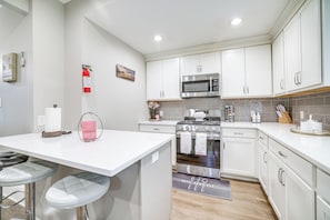 A modern kitchen with white cabinets, stainless steel appliances, and a bar area with stools.