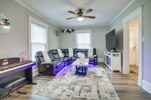 A living room with a sectional sofa, a piano, a ceiling fan, and a television.