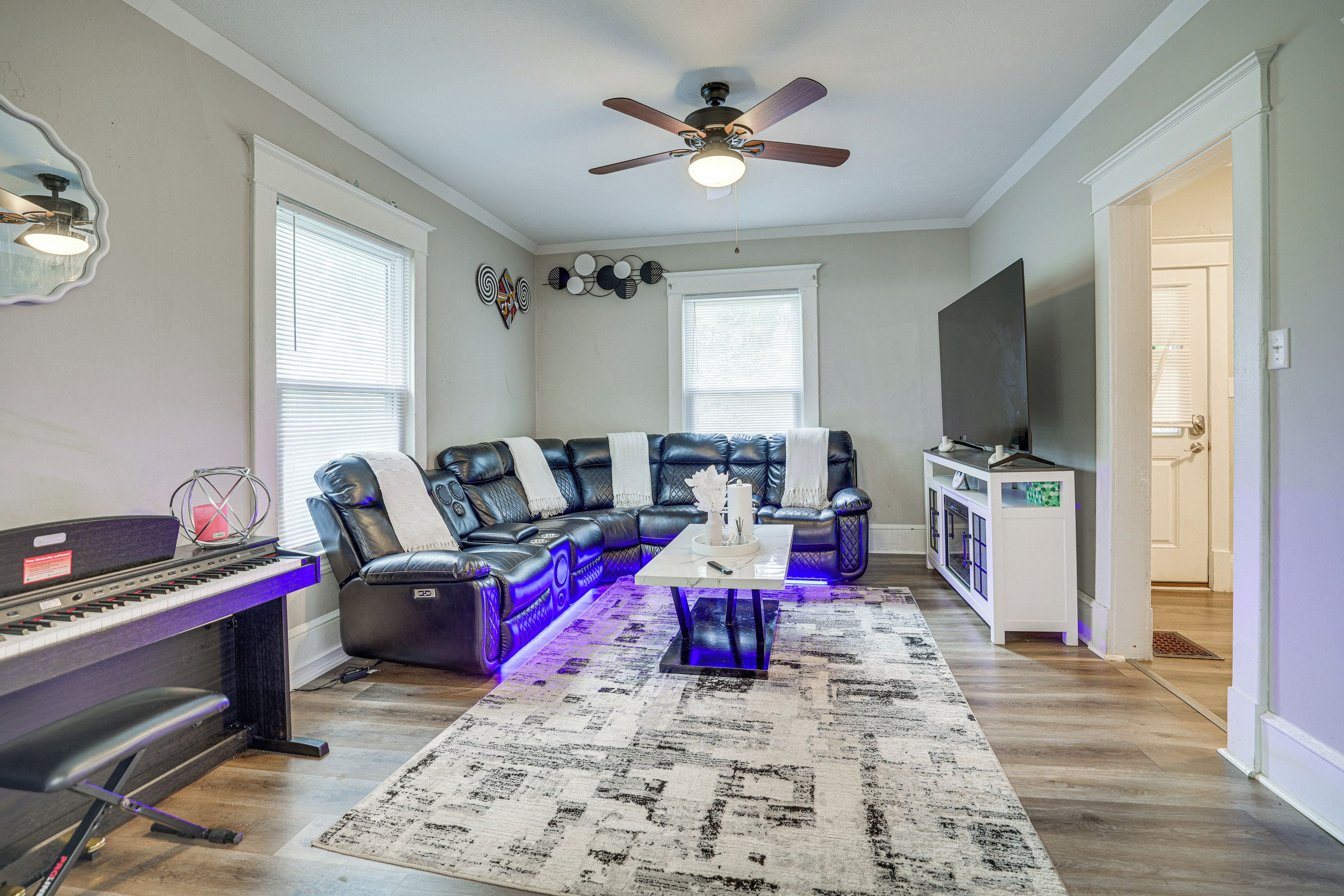 A living room with a sectional sofa, a piano, and a ceiling fan.