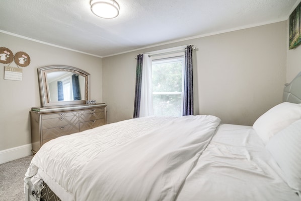 A bedroom with a bed, dresser, mirror, and window with curtains.