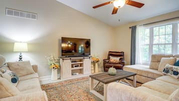 A living room with a ceiling fan, a television, a sofa, a chair, a coffee table, and a window with curtains.