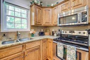 A kitchen with wooden cabinets, a stainless steel stove, a microwave, and a sink. - Screened Porch, Fire Pit! Family Home Near K-state (Manhattan)