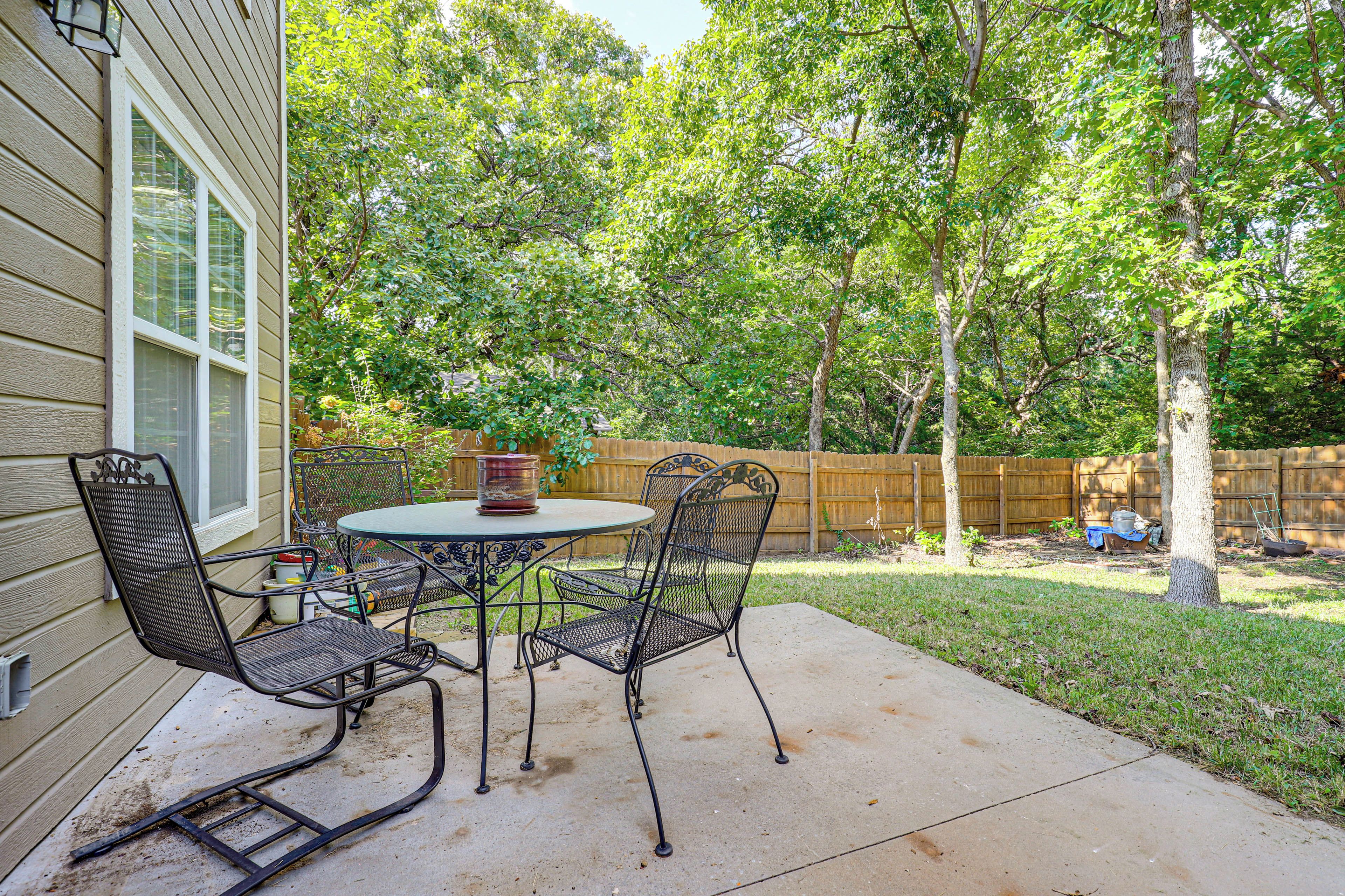 An outdoor patio with a round table and four chairs, surrounded by a wooden fence and trees.