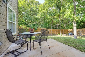 An outdoor patio with a round table and four chairs, surrounded by a wooden fence and trees.
