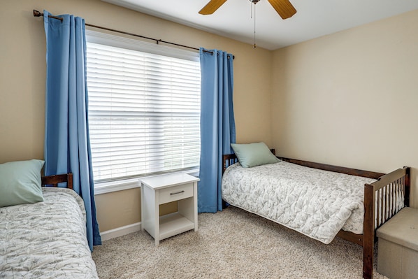 A bedroom with two single beds, a nightstand, a window with blinds, and a ceiling fan. - Screened Porch, Fire Pit! Family Home Near K-state (Manhattan)