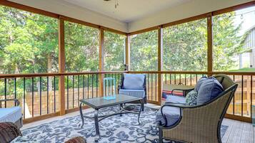 A covered patio with a table and chairs, a ceiling fan, and a view of trees.