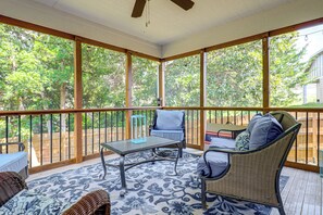 Varanda coberta com mesa, cadeiras e um ventilador de teto, com vista para árvores.