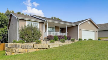 A two-story house with a covered front porch, a garage, and a stone retaining wall.