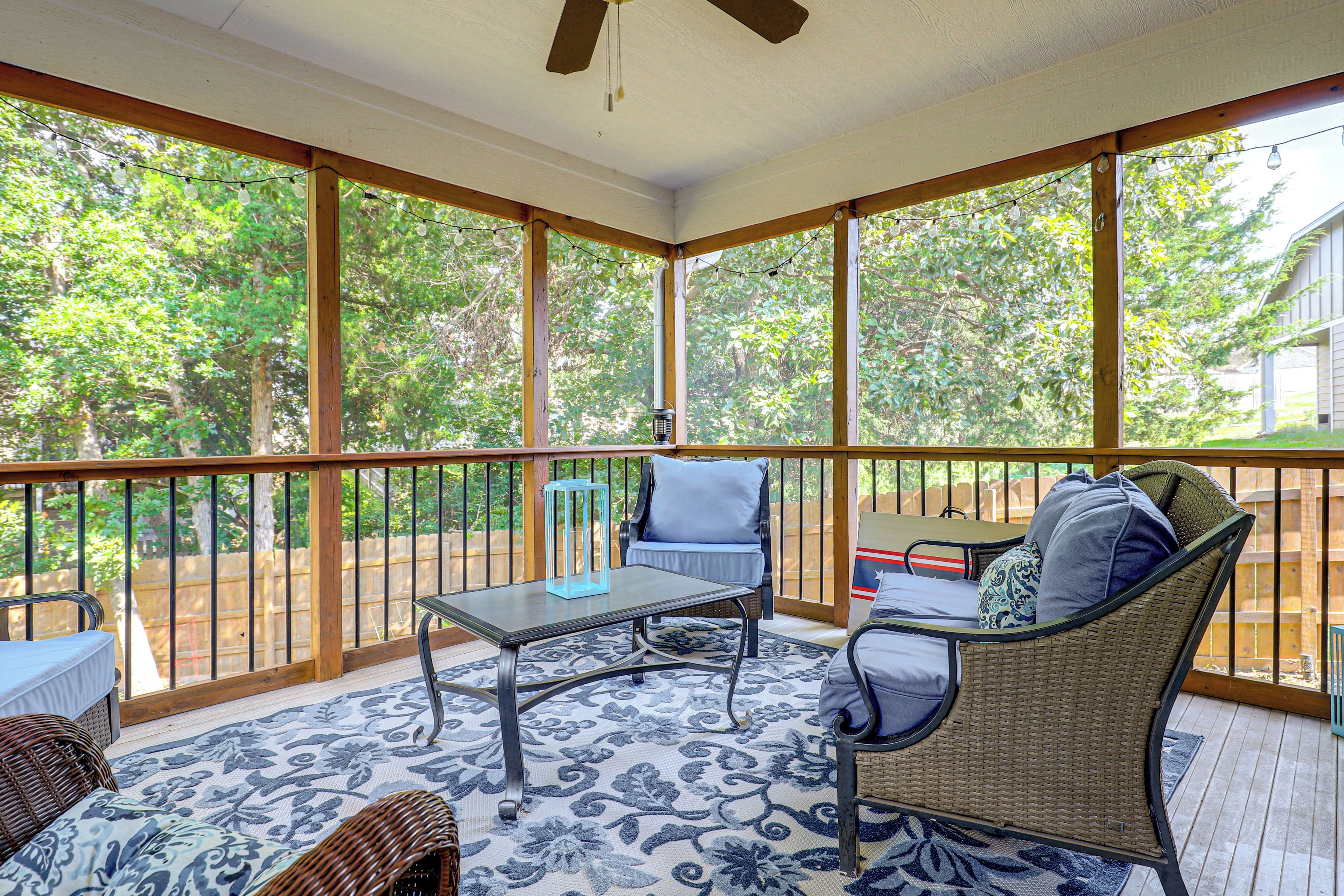 A covered patio with a table and chairs, a ceiling fan, and a view of trees.