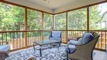 A covered patio with a table and chairs, a ceiling fan, and a view of trees.