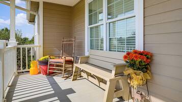 A porch with a wooden bench, a chair, and a potted plant.