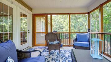 A covered porch with a seating area, including a chair and a sofa, and a table.