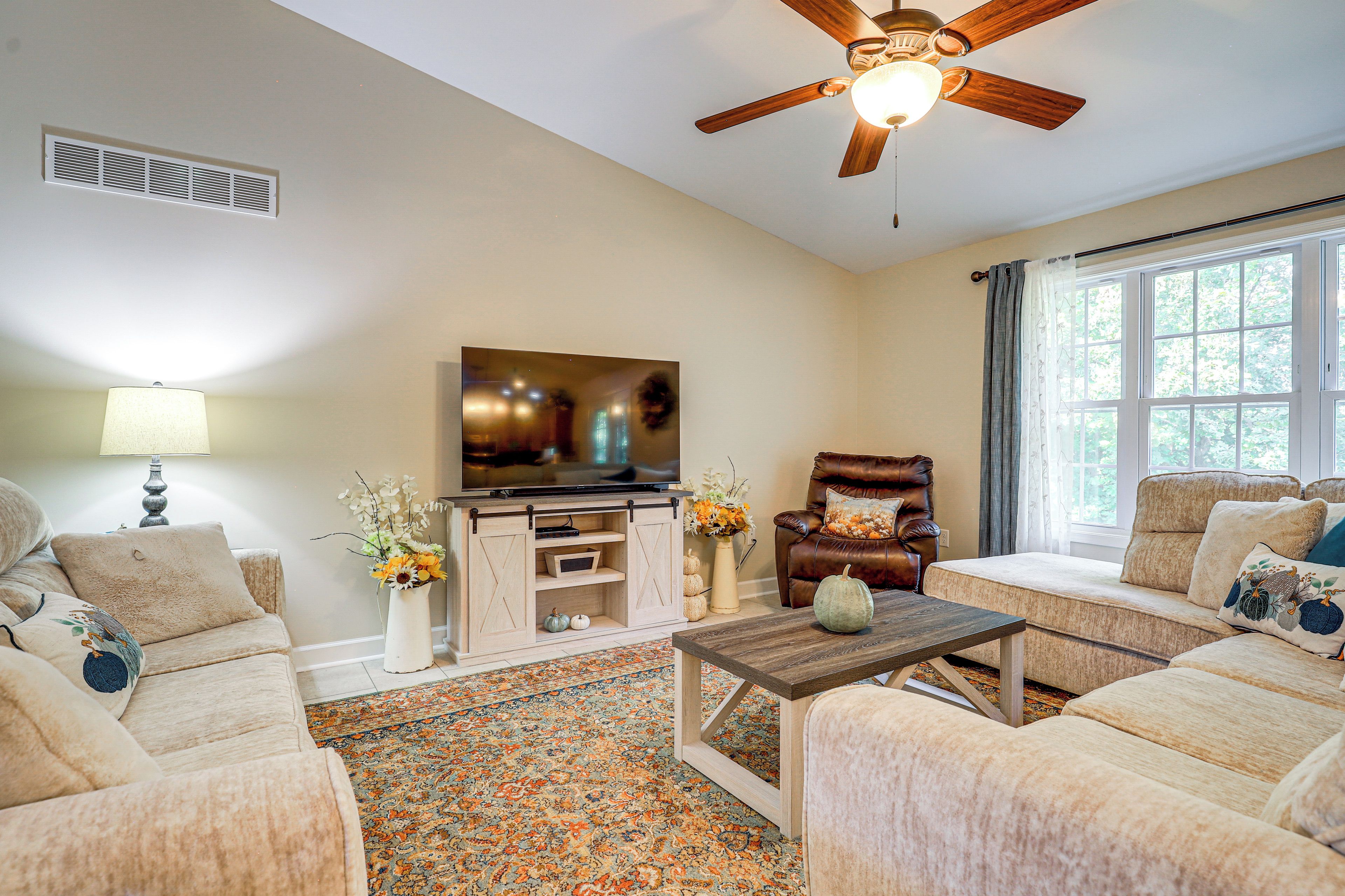 A living room with a ceiling fan, a television, a sofa, a chair, a coffee table, and a window with curtains.