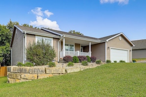 A two-story house with a covered front porch, a garage, and a stone retaining wall. - Screened Porch, Fire Pit! Family Home Near K-state (Manhattan)