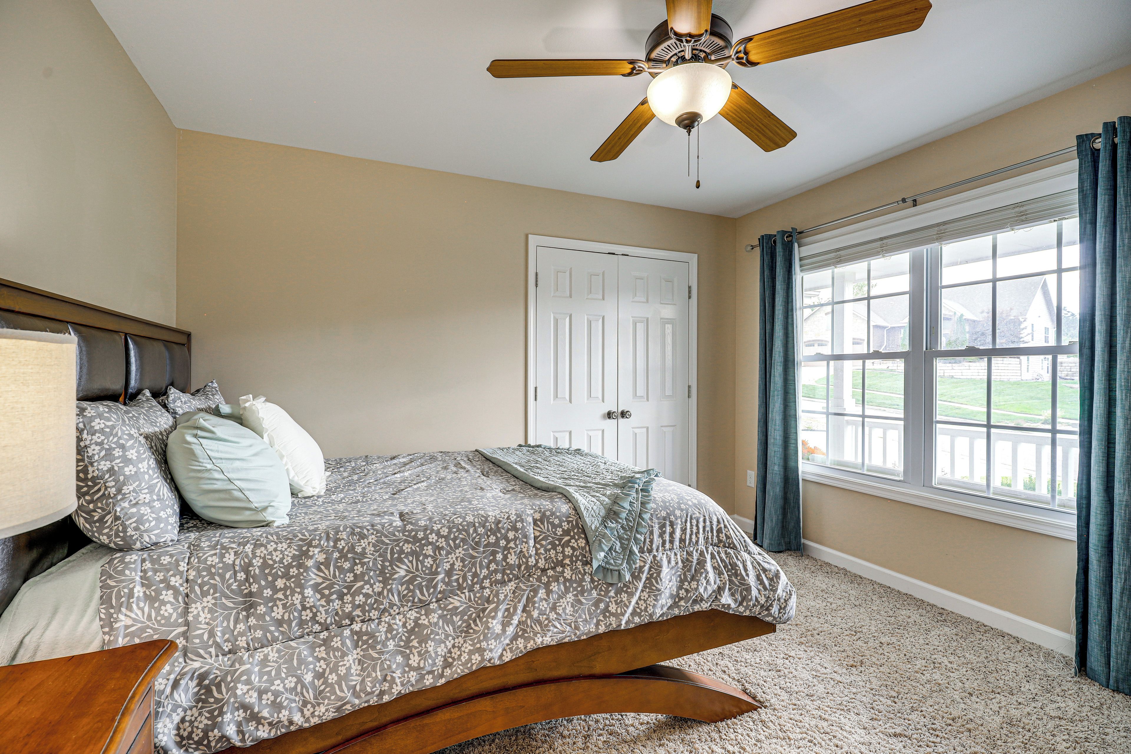 A bedroom with a bed, a ceiling fan, a window with curtains, and a door.