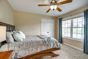 A bedroom with a bed, a ceiling fan, a window with curtains, and a door.