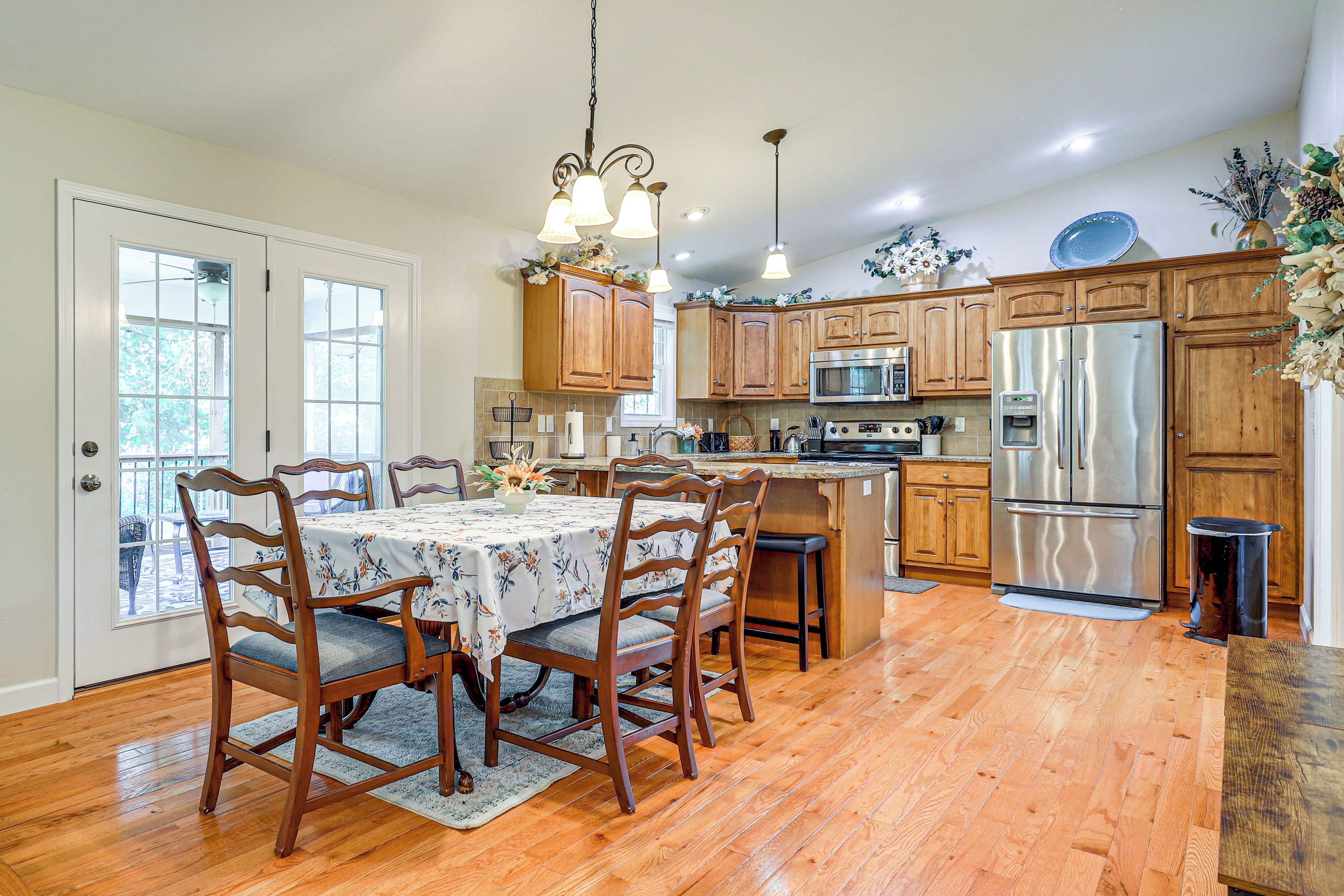 A kitchen with wooden cabinets, stainless steel appliances, a dining table with chairs, and a hanging light fixture.