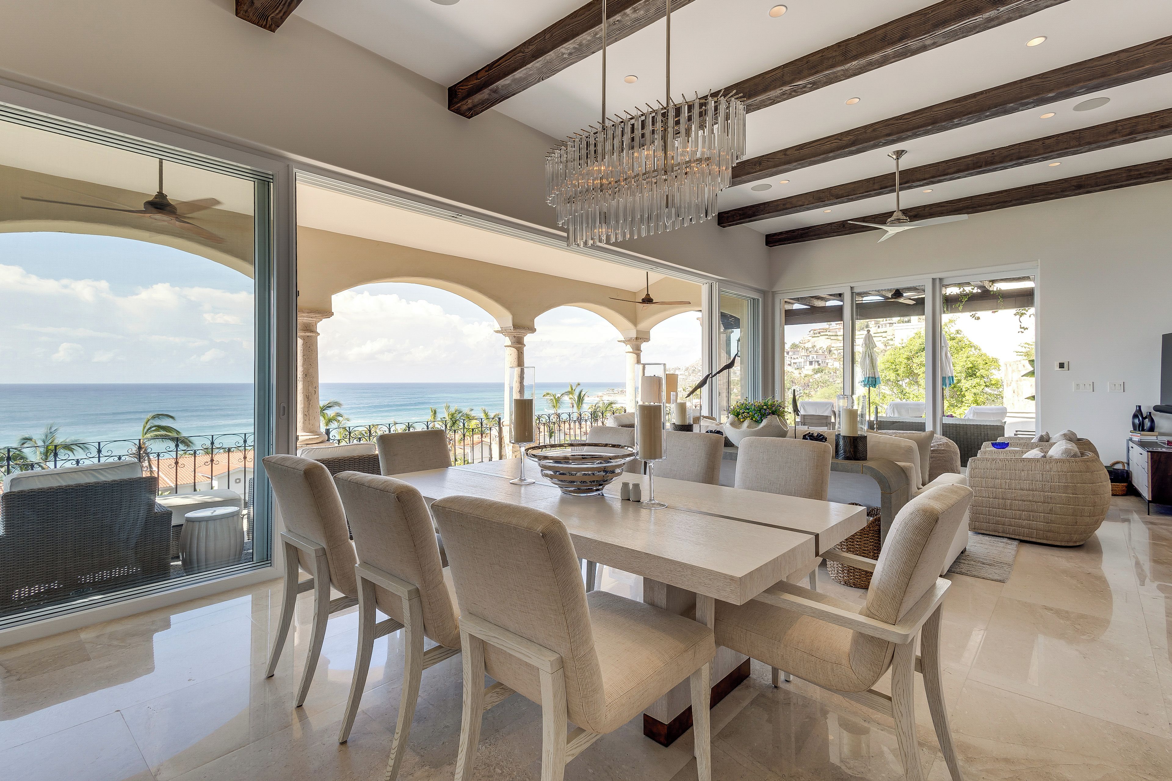 A spacious living area with a view of the ocean, featuring a dining table, chairs, and a chandelier.