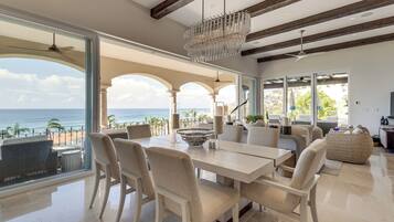 A spacious living area with a view of the ocean, featuring a dining table, chairs, and a chandelier.