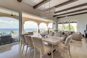 A spacious living area with a view of the ocean, featuring a dining table, chairs, and a chandelier.