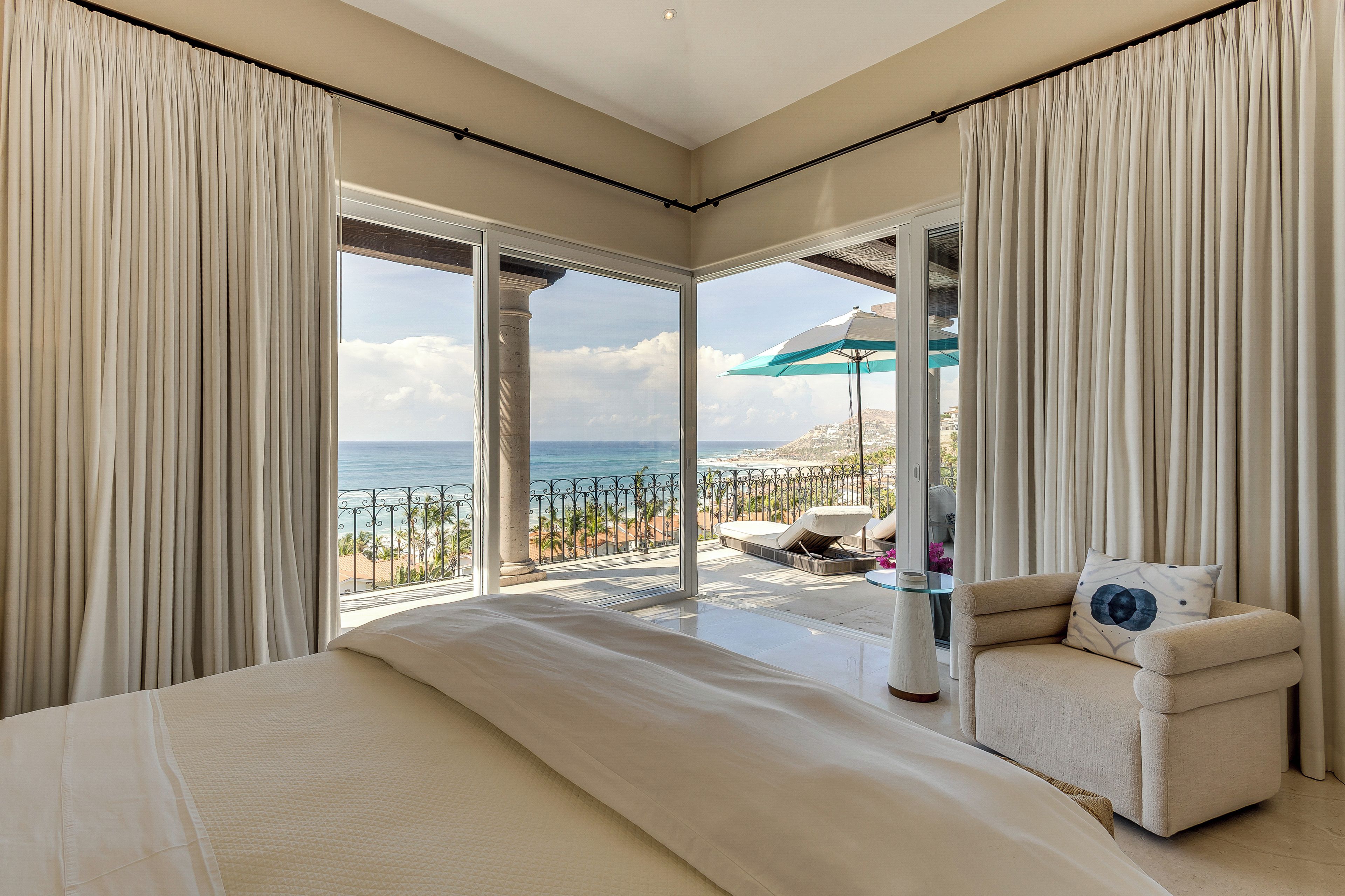 A bedroom with a large bed, a sofa, and a balcony with a view of the sea.