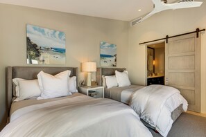 A hotel room with two beds, a nightstand with a lamp, a large mirror, and artwork on the walls.