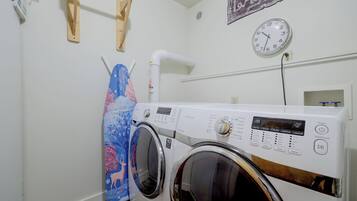 A laundry room with a front-loading washing machine, a wall-mounted clock, and a wooden drying rack.