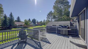 A deck with a grill and outdoor furniture, overlooking a residential area with houses and trees.