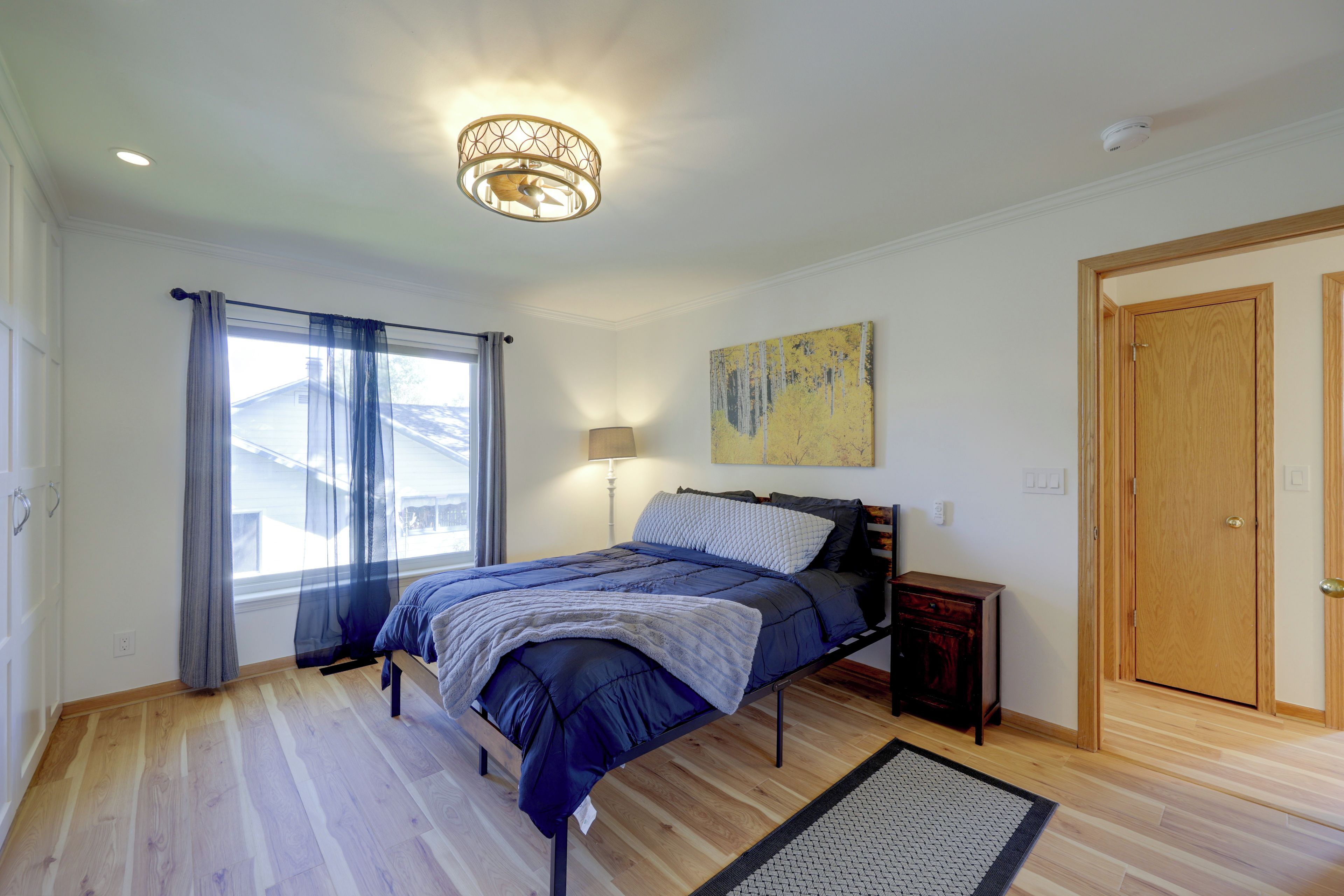 A bedroom with a bed, a bedside table, a lamp, a painting, and a door.