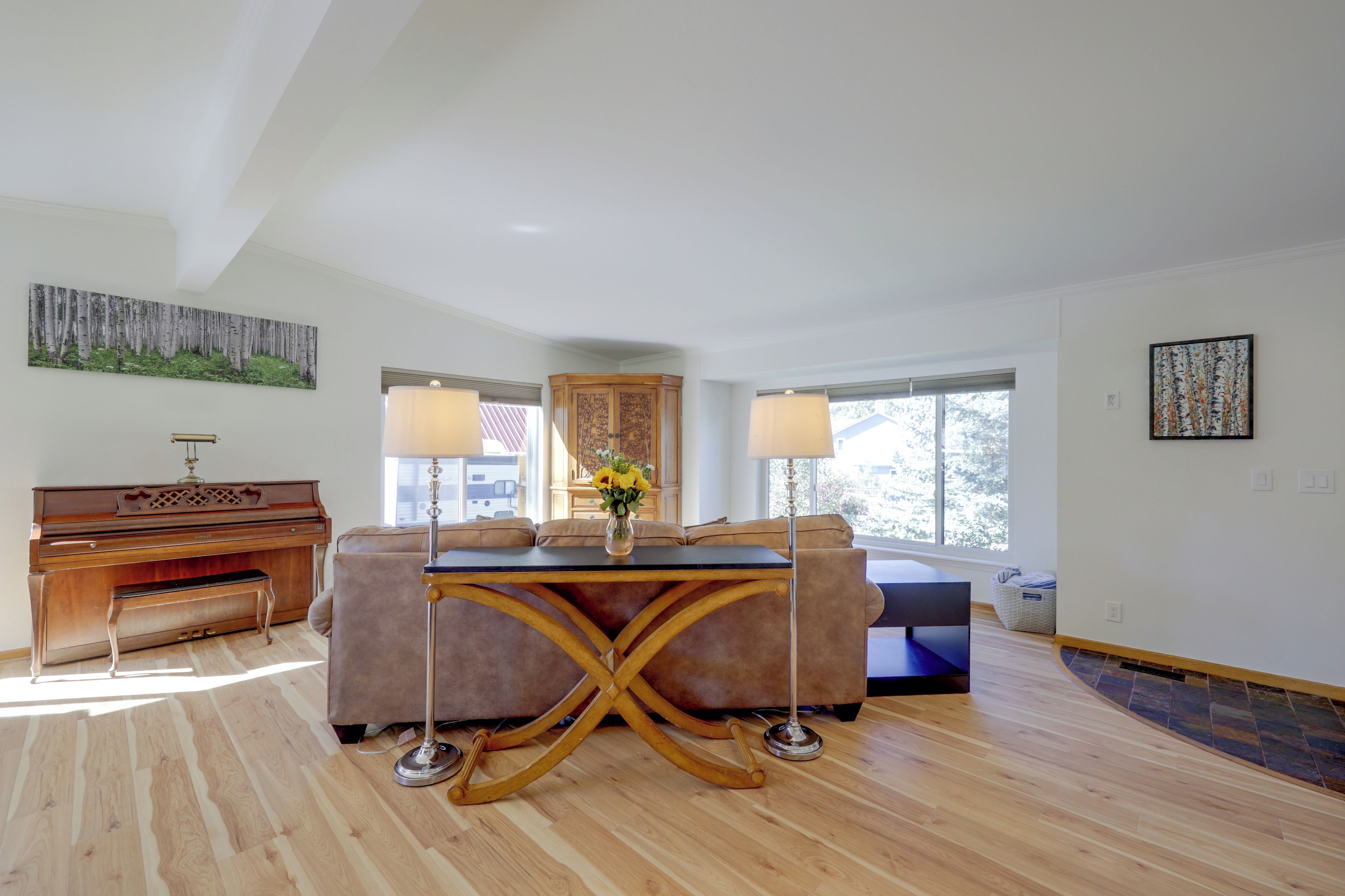 A spacious living room with a piano, a sofa, a coffee table, and a large window.