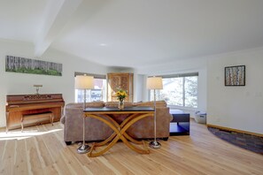 A spacious living room with a piano, a sofa, a coffee table, and a large window. - Private Sauna at Family-friendly Eagle Home W/deck (Eagle)