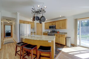 Una cocina moderna con una isla central, electrodomésticos de acero inoxidable, armarios de madera y vistas al exterior.