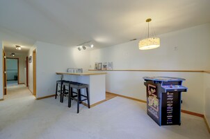 Una habitación con área de cocina, un taburete de bar, una mesita y una máquina arcade de Pac-Man.