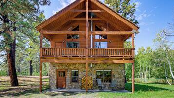 A two-story log cabin with a balcony, stone foundation, and outdoor seating area.