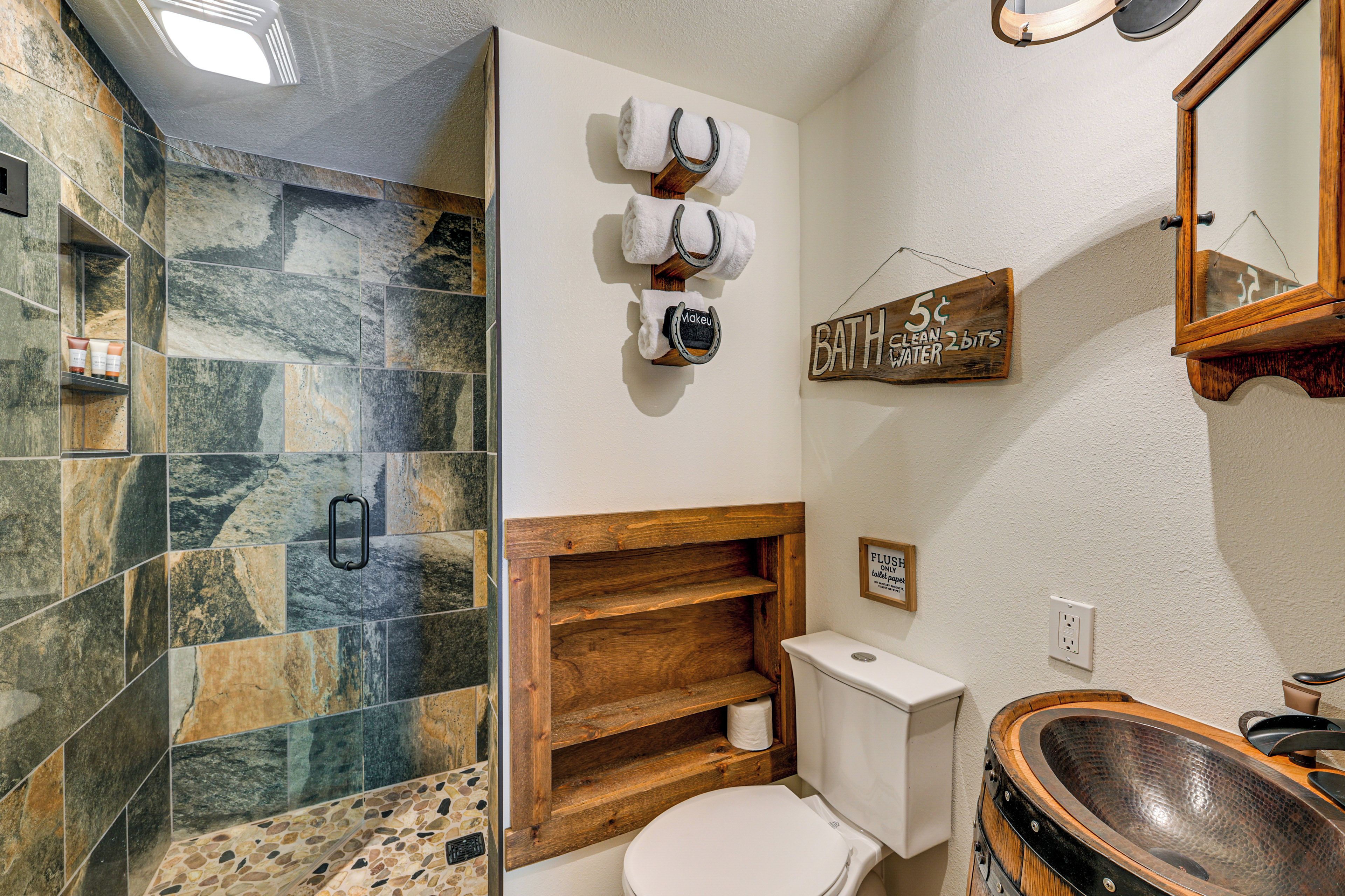 A bathroom with a stone shower, a wooden shelf, a toilet, and a basin.
