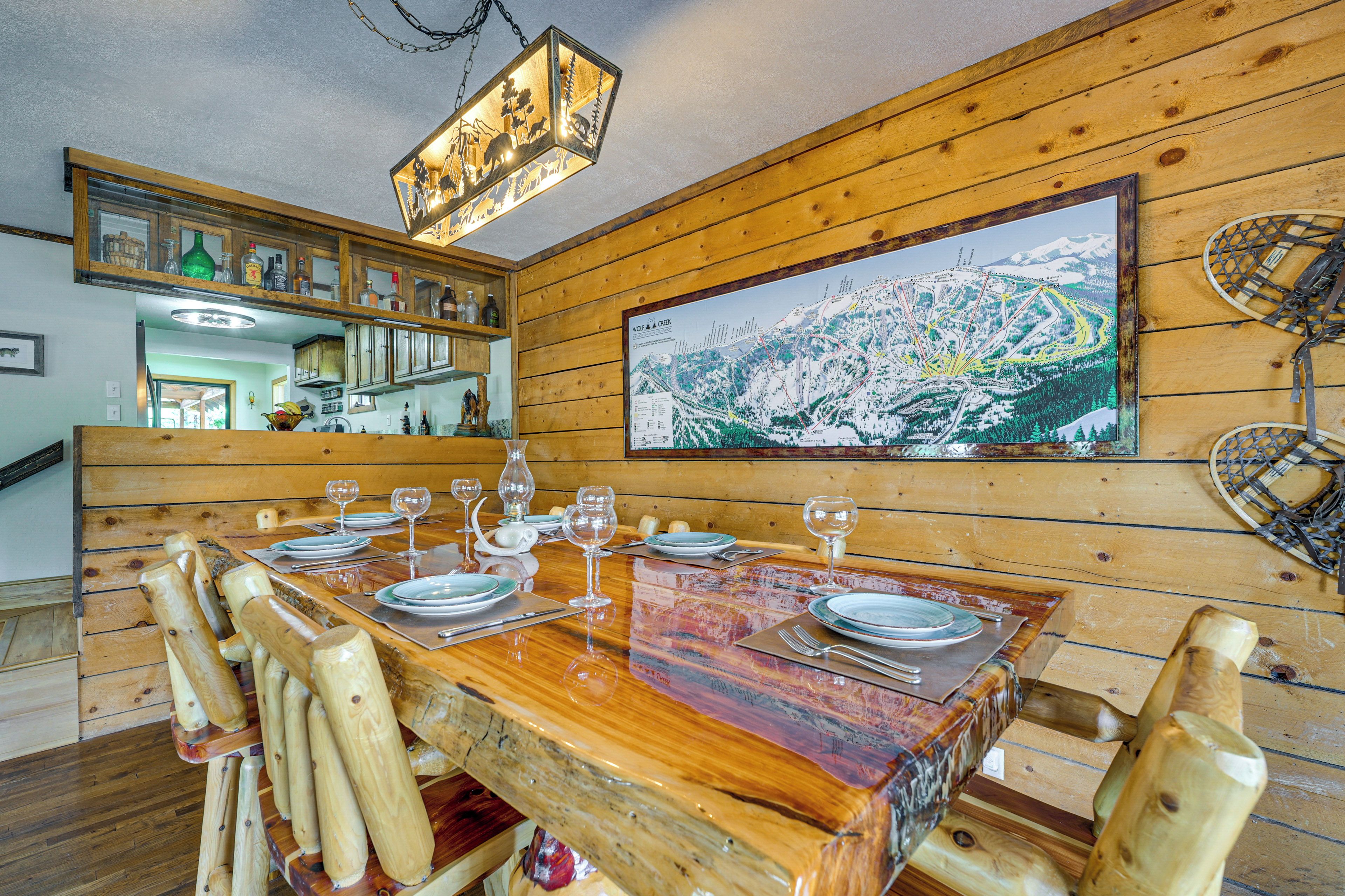 A wooden dining table set with plates, glasses, and cutlery, surrounded by wooden chairs.