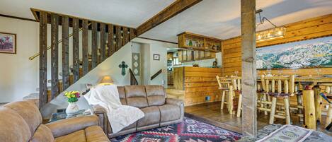 Un interior rústico con una escalera de madera, un rincón de estar acogedor con un tapete estampado y un comedor con sillas de madera.