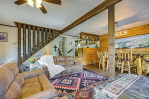 A rustic interior with a wooden staircase, a dining area with wooden chairs, and a living room with a sofa and patterned rug. - Ski, Soak & Play at Littlefoot Cabin w/ Game Room (Pagosa Springs)