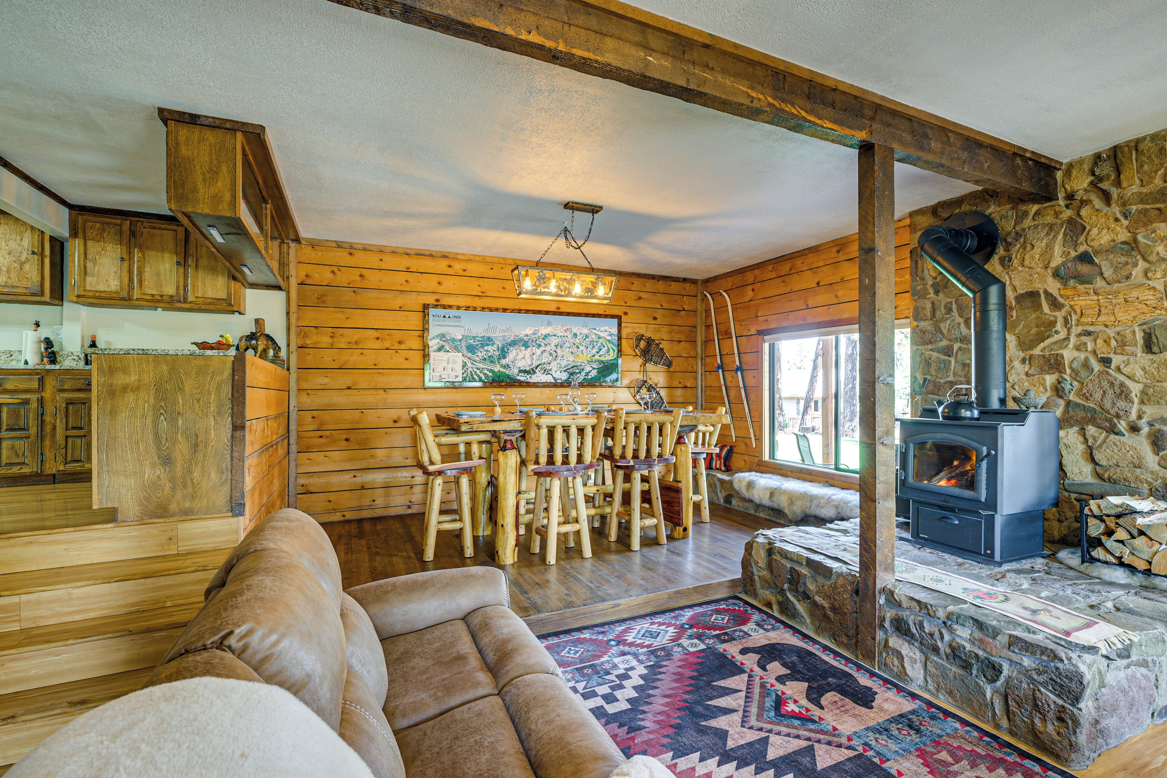 A rustic cabin interior with a stone fireplace, wooden furniture, and a dining area.
