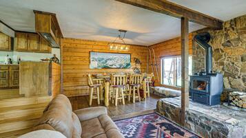 A rustic cabin interior with a stone fireplace, wooden furniture, and a dining area.