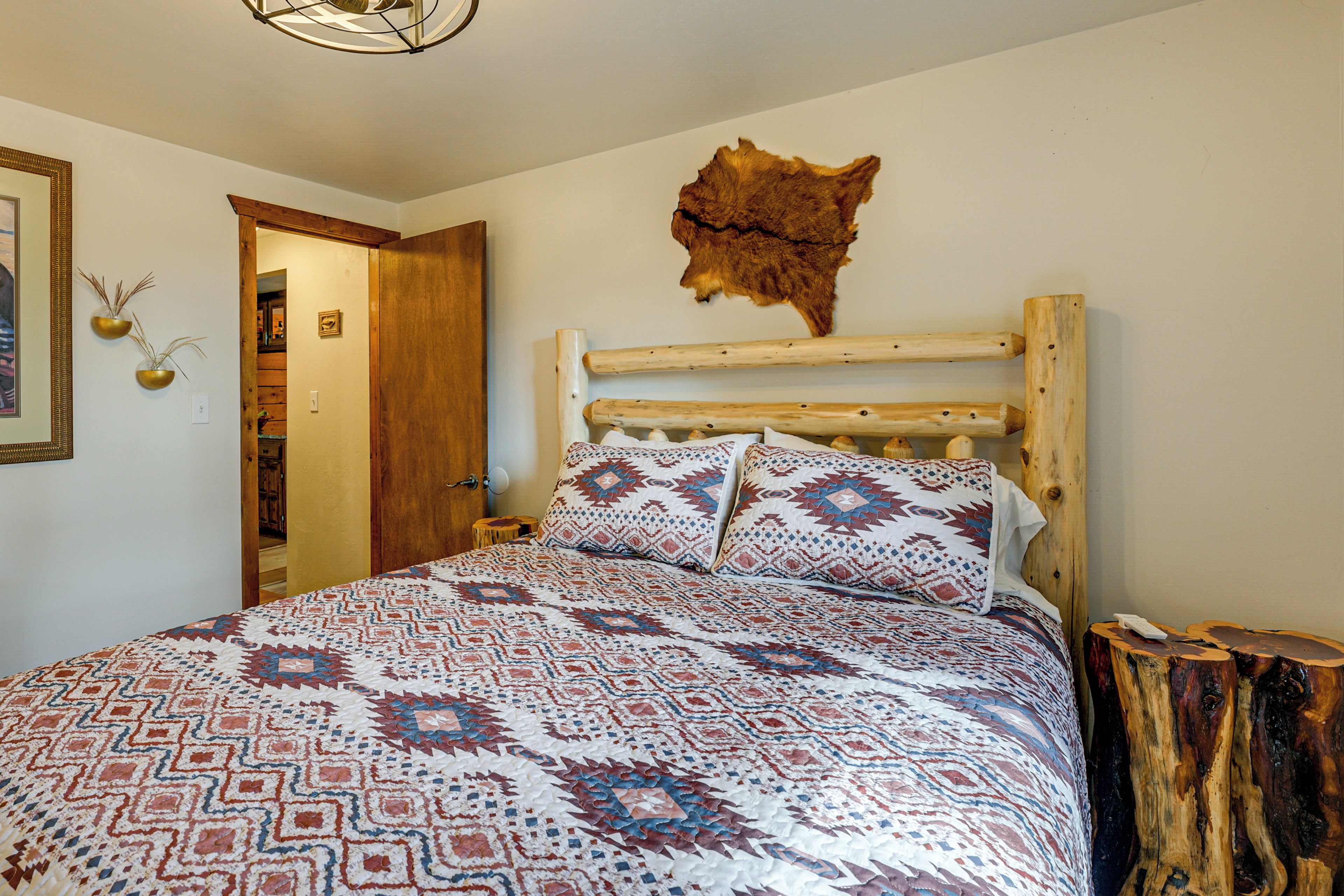 A bedroom with a patterned bedspread, a wooden headboard, and a wall-mounted animal hide.