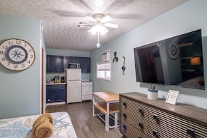 A compact living space with a kitchenette, a bed with a star-patterned cover, a ceiling fan, and a television. - Hot Tub & Dock Access! Bayfront Studio (Fort Walton Beach)