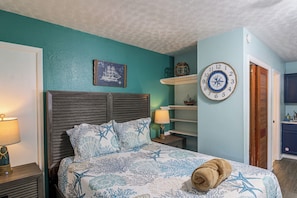 A bedroom with a bed, a wall clock, a shelf with a ship model, and a door. - Hot Tub & Dock Access! Bayfront Studio (Fort Walton Beach)