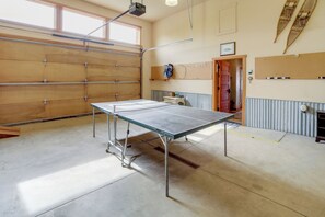 A ping pong table in a room with a garage door, a pegboard, and a door leading to another room.