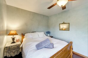 A bedroom with a bed, a nightstand, a lamp, a ceiling fan, and a wall-mounted mirror.